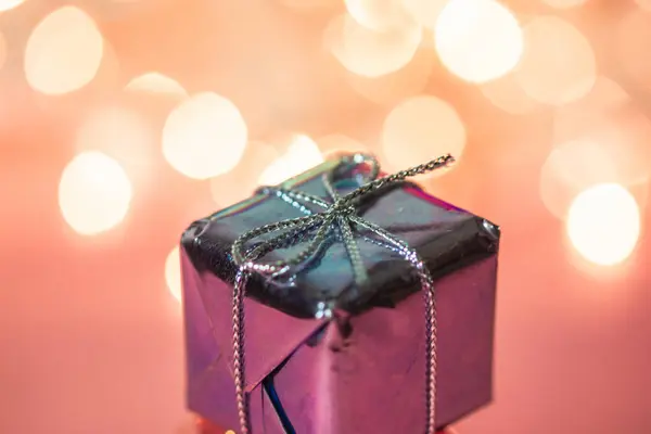 Small silver pink gift box on warm gradient background and spot lights. Holidays greetings. Merry Christmas and Happy New Year 2024. Wrapped present for Valentines day, February 14. Black Friday sales