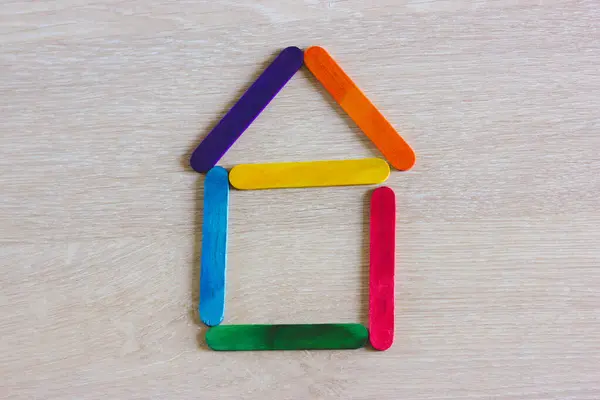 Symbolic toy house built from wooden colorful play sticks top view. Hometown real estate, home buying and renting concept. Bright colors house shape. Home made of wood ice lolly sticks on wooden table