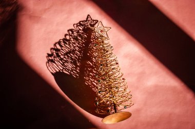 Pembe masanın tepesinde altın yıldızlı dekoratif Noel ağacı gölge yapar. Yeni yıl 2024. Kutlama kutlaması. Kış tatili, 31 Aralık.