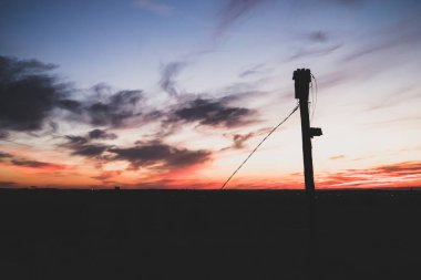 Bulutlu gün batımına karşı elektrik hattı silueti. Elektrik kablosu. Elektrik, güç üretimi, enerji konsepti. Alacakaranlıkta yüksek voltaj. 
