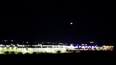 Geceyle birlikte soyut bulanık arkaplan. Bulanık ışıkların ufukta belirdiği şehir. Arabalar hareket ediyor. Havaalanından kalkan uçaklar.