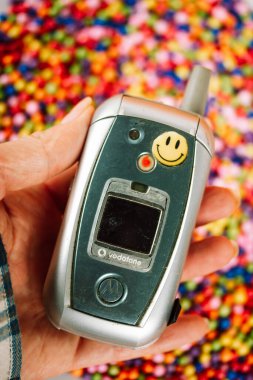 Madrid, İspanya. 2 Ocak 2024 Eski Motorola telefonu. Kadının elinde gülen surat etiketi var. 90 'lar ve 00' ler için nostalji. El ele tutuşma klasik telefon..