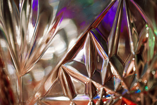 Abstract lead diamond-shaped crystal in sunlight. Beautiful rippled glass. Close up view of a glass vase illuminated with colorful multicolored light.