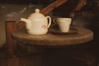 Kahverengi mutfak tasarımı. Masa takımı. Seramik bej çaydanlık ve kafedeki ahşap yuvarlak masa üzerinde duran iki fincan. Lokanta, Dark Key yemek ve içecek fotoğrafı. Sabah kahvaltısı. Geleneksel çay partisi