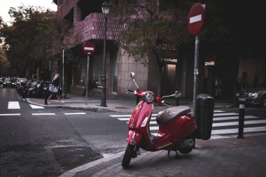 Madrid, İspanya. 19 Kasım 2023 Red Piaggio Vespa scooter 'ı şehir sokağına park etti. Çevre dostu eski model nakliye aracı. Avrupa şehir sokağı. Beyaz yaya geçidi, zebra. Şehir manzarası. Seyahat fotoğrafı.