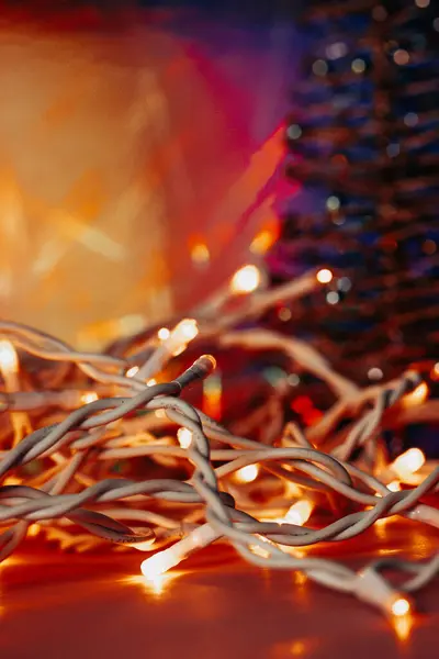 Tangled white wires LED garland for Christmas tree selective focus. New Year 2024 home decor. Warm lights on bright orange background. Abstract details of decorated home for celebration New Year\'s eve