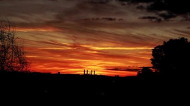 Gün batımında şehir manzarasının üzerinde güzel, ateşli kırmızı gökyüzünün hızlandırılmış videosu. Gün akşama ve geceye dönüşür. Turuncu bulutlar karanlıkta ufuk çizgisinde hızla yüzerler. Karanlık, siyah ve kırmızı soyut manzara