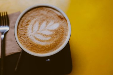 Retro filtre efektli sarı bir masada bir fincan sanat latte ya da cappuccino kahve. Kahvaltının üstünde sıcak içecek var. Bardakta sonbahar içkisi. 