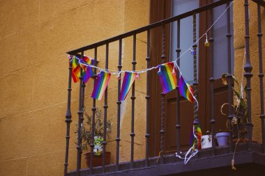 Gökkuşağı renkli LGBT bayraklarıyla süslenmiş bir balkon. Sıcak turuncu ev. Evin dış detayları. Avrupa 'da gurur ayı. Eşcinsel mahallesi .