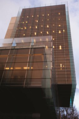 Ilık ışıklandırması olan yüksek bir iş binasının mavi cam cephesi. Ofis binalarının pencereleri. Şehir sokağı. Şehir manzarası. Şehir manzarası. Ön cam parlatıcısı