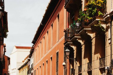 Eski şehir caddesi perspektifi. Balkonlarda yeşil saksı bitkileri olan kırmızı ev cephesi. Gün ışığında dış bina ve şehir caddesi perspektifte. 