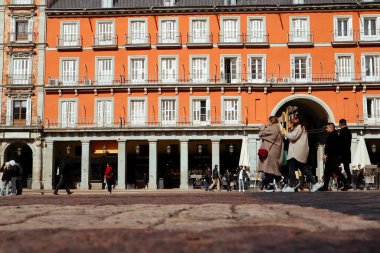 Madrid, İspanya, 27 Şubat 2024 güneşli bir günde İspanya 'nın başkentinde Plaza Mayor' da yürüyen insanlar. Turuncu tarihi bina cephesi. Düşük açılı fotoğraf