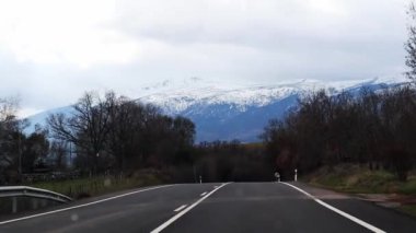 Güneşli kış günlerinde karla kaplı tepeleri olan dağlara giden boş asfalt bir yol. Kış zamanı dağlarda bir yolculuk. Ön araba penceresi gezisi. 