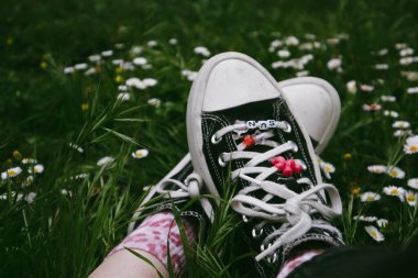 Madrid, İspanya. 7 Ocak 2024. Kadınların ayaklarındaki klasik Converse ayakkabıları. Eski ayakkabılar ve yeşil çimenler. 90 'lar için nostalji. Ormanda dinlenen bir kız..