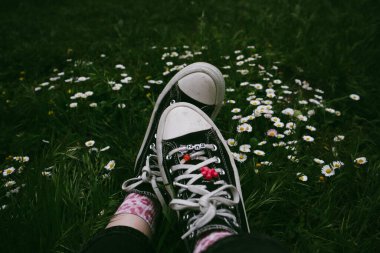 Madrid, İspanya. 7 Ocak 2024. Kadınların ayaklarındaki klasik Converse ayakkabıları. Eski ayakkabılar ve yeşil çimenler. 90 'lar için nostalji. Ormanda dinlenen bir kız..