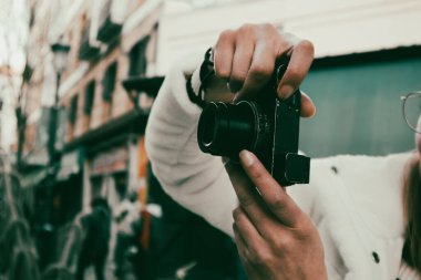 Madrid, İspanya. 1 Mart 2024. Beyaz önlüklü genç bir kadın, şehir sokaklarında gezen kadın fotoğrafçı hobisi olan küçük bir dijital kamerayla fotoğraf çekiyor.