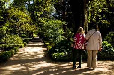Madrid, İspanya. 7 Nisan 2024 İlkbahara adım at. Kadınlar bahçede geziniyor, park ediyor. Verdant Patikası bir perspektifte ilerliyor. Yeşil ağaçların gölgeleri.