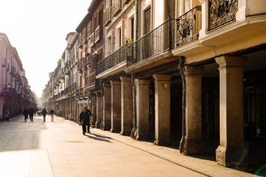 Alcala de Henares, İspanya. 30 Ocak 2024. Sıcak güneş ışığıyla dolu eski bir şehir caddesi. Antik İspanyol mimarisi. Bakış açısında vintage sütunları. 