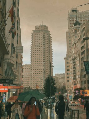 Madrid, İspanya. 1 Eylül 2023 dikey şehir manzarası, yüksek apartmanlar, yağmurlu günlerde gökdelenler. Şehir sokaklarında şemsiyeli insanlar.