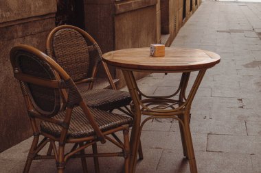 Madrid, İspanya. 1 Mayıs 2024 Bir ahşap yuvarlak masa ve kafeteryada iki hasır rahat sandalye, restoran terasında. Dinlenmek için rahat bir yer, randevu. Şehir sokağı.