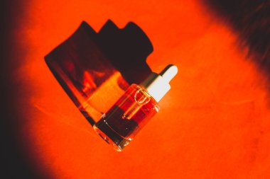 Kırmızı yüzey manzarasında duran cam kozmetik pipo şişesinin bir kopyası. Masadaki serum şişesinin zıt gölgesi. Kadın günlük güzellik rutini. 