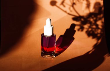 Sarı arka planda yüz bakımı için serumla birlikte cam kozmetik şişesi. Kadın güzellik ürünü. Doğal zemin üzerinde serumlar ve bitkilerin gölgeleri..