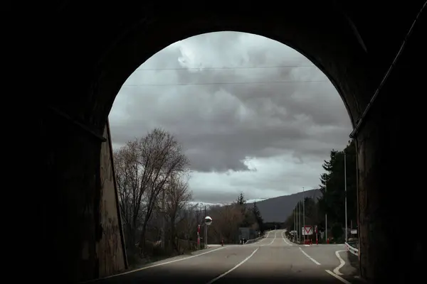stock image Empty asphalt road passing through an arch-shaped tunnel. Dark dramatic travel photography. Traveling in a cold day Gloomy landscape with rainy clouds