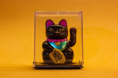 Maneki Neko Japon şanslı kedisi sarı turuncu arka planda patisini sallıyor. Çin iyi şans sembolü. Kitty 'e hoş geldin hediyesi. Başarı oyuncağı.