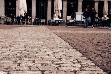 Madrid, İspanya. 1 Mart 2024 Kafe terasında masalar, eski şehir caddesinde şemsiyeler antik taş kaldırımlar, Granit kaldırımlarında yürüyen insanlar.