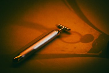 Soyut koyu sarı arka planda altın bir elektrikli yüz masajcısı. Güzellik tedavisi yaşlanmayı önleyici ürün modeli. Kadın rutin aracı