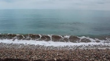 Mavi turkuaz okyanus dalgaları. Akdeniz kıyı şeridi manzarası. Kasvetli bir günde çakıl taşları olan bir kumsal. Kıyıdaki volkanik siyah kum, soğuk su.