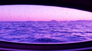Akşamları dalgalarla dolu yatın penceresinden deniz manzarası. Mor pembe günbatımı gökyüzü. Su taşımacılığıyla seyahat ediyor. Pencereye su damlıyor.