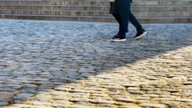 Yaya ayakları ve kaldırımlı bir yolda uzun gölgeler. Şehir sakinleri, gün batımında şehir caddesinde yürüyen tanınmayan insanlar. Yavaş çekim.