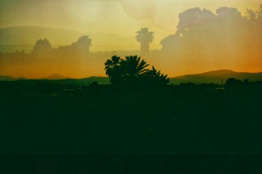 Tropik manzara dağları, gün batımında ufuktaki tepeler. Çifte maruziyet. İspanyol manzaraları, vahşi doğa. Palmiye ağaçları siluetleri. Film filtresi fotoğrafı.