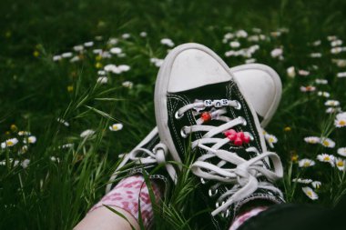 Madrid, İspanya. 7 Ocak 2024. Klasik Converse kadın ayaklı spor ayakkabıları. Eski ayakkabılar ve yeşil çimenler. 90 'lar için nostalji. Ormanda dinlenen bir kız..