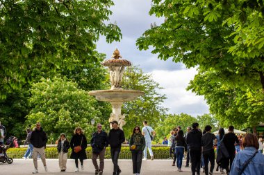 Madrid, İspanya. 2 Mayıs 2024 Bir bahar botanik bahçesinde şehir caddesinde yürüyen bir kalabalık. Dışarıda vakit geçirmek. Antika çeşme simgesi. 