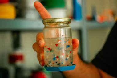 Colorful plastic parts floating inside of a bottle in a hand. Separating plastic by type in a laboratory. Zero waste laboratory. Separation process.  clipart