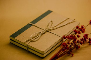 Kraft vintage doğal, basit kahverengi karton defter kahverengi masanın üzerinde. Ekolojik kurdeleli kağıt günlük ve kırmızı küçük çiçek buketi. Yaz anıları. 