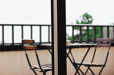 Ahşap masa ve panoramik pencerenin arkasındaki balkonda sandalyeler. Evdeki bahçe mobilyaları. Ormandaki bir evde boş bir teras. Terasta parmaklıklar.