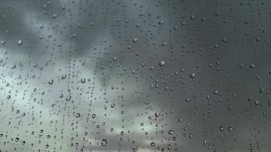 Yağmurlu, kasvetli bir günde ıslak bir pencerede su damlıyor. Sonbahar gününde doğayla ilgili soyut bir video. Yağmur damlaları yavaşça düşüyor. Sonbahar mevsiminde yağmur. 