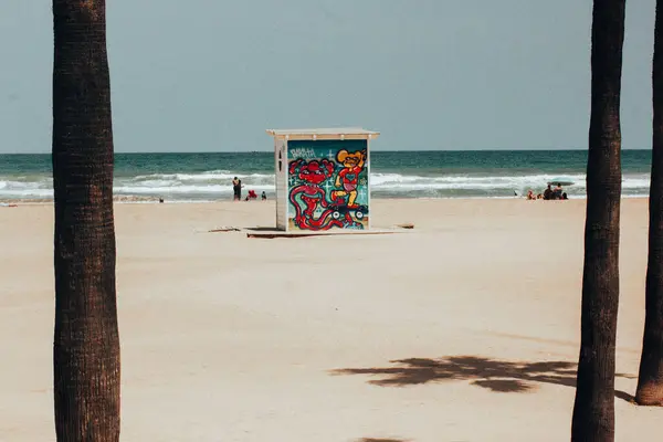 stock image Gandia, Spain. 1 June 2024 Changing room with bright graffiti on a facade. White sandy beach, shadows from palm trees and blue sea. Summer vacation.