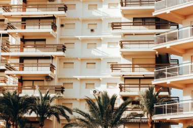 Çağdaş, çok katlı, balkonlu, güneşli gün ışığında pencereli bir apartmanın bej rengi cephesi. Palmiye ağaçları. Tropik tatil köyü. Deniz kenarındaki ev.. 