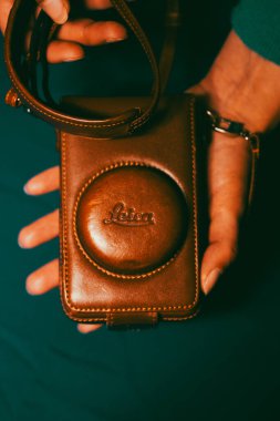 Madrid, Spain. 1 May 2023 Vintage Leica camera in brown leather case lying in female hands on blue background. Retro photography hobby. Photographer.