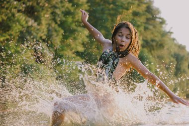 Happy teenage girl of European-Asian appearance 10-13 years old in a jump. A child is frolicking having fun swimming in a river, lake, sea on summer vacation. Happy childhood. Skinny athletic girl.