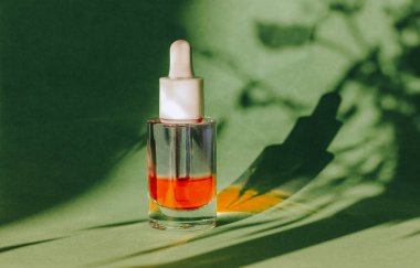 Yeşil arkaplanda kırmızı yüz serumu kavanozu ve bitki kontrastı gölge deseni. Vücut bakımı için kozmetik ürünleri. Kütikül yağı. Pipetli kozmetik şişesi. Günlük rutin. Şık kozmetik ürünler.