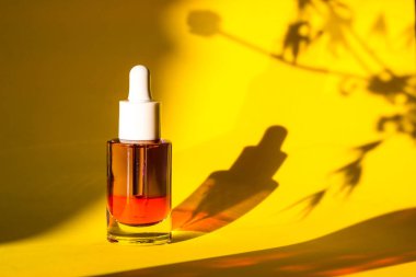 Sarı arka planda yüz ve vücut bakımı için serumu olan cam kozmetik kavanozu. Kadınlar için bakım ürünleri. Kadın güzellik aleti ve kozmetik. Bitkilerin gölgeleriyle doğal arkaplanda yüz serumu.