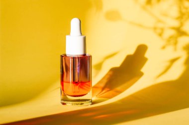 Sarı arka planda yüz ve vücut bakımı için serumu olan cam kozmetik kavanozu. Kadınlar için bakım ürünleri. Kadın güzellik aleti ve kozmetik. Bitkilerin gölgeleriyle doğal arkaplanda yüz serumu.