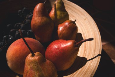 Güneşli bir günde tahta bir kasede olgun kırmızı armutlar ve mavi üzümler. Yaz ya da sonbahar meyveleri. Güneş ışığında otantik bir hayat. Multivitamin yiyecekler..