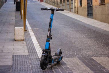 Madrid, İspanya. 1 Mayıs 2023 Cabify mavi elektrikli scooter bir şehir caddesine park edilmiştir. Ekolojik şehir ulaşımı. Eski kasabadaki kaldırım taşı yolu. 