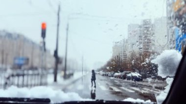 Soğuk kış havasında kırmızı ışıkta duran bir araba, yayaların zebrayı geçmesine izin veriyor. Silecekler kar ve yağmurdan ön camı temizler..